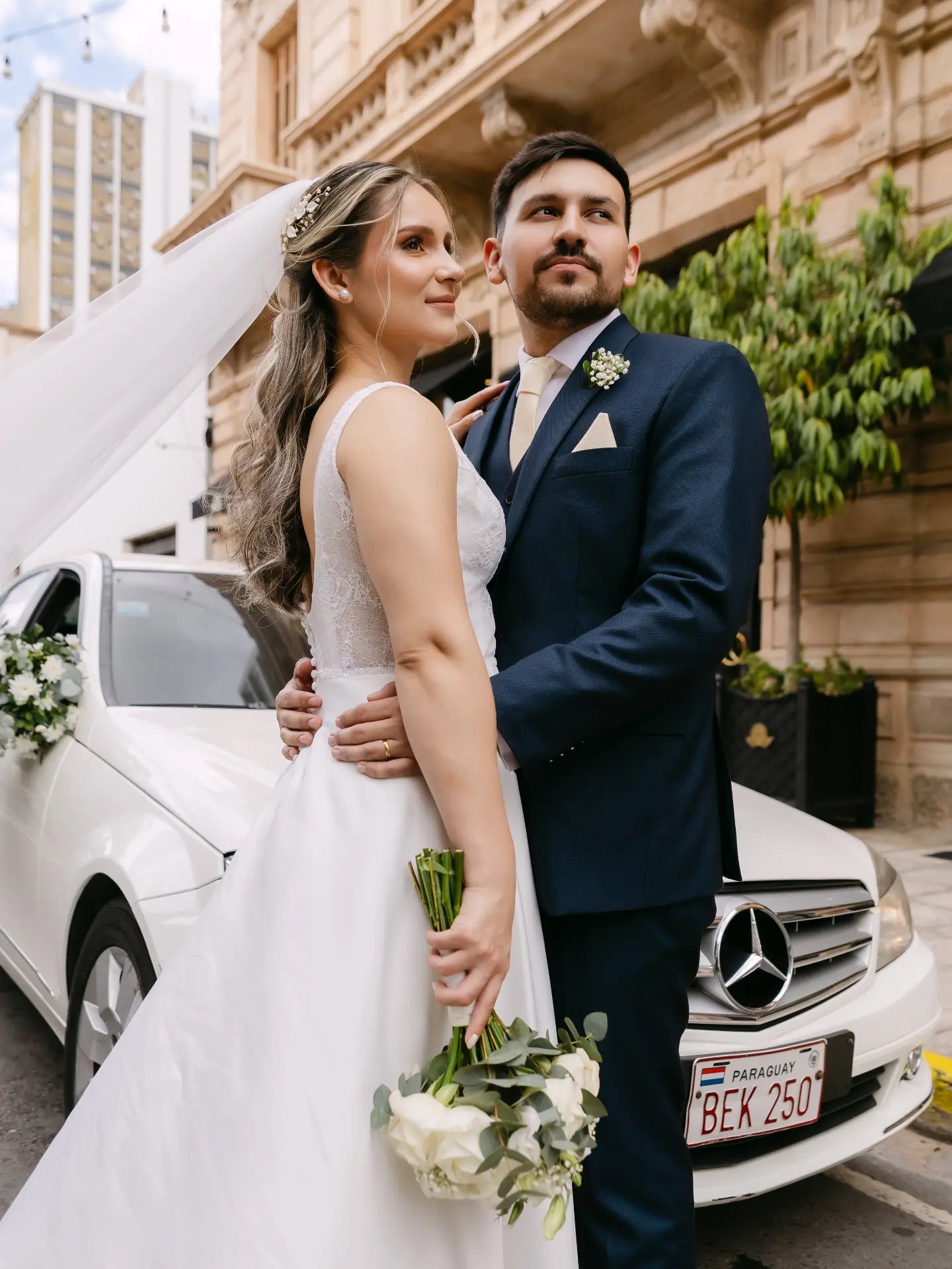 Novios abrazados junto al auto de la boda, vestido Melisa Sebeca